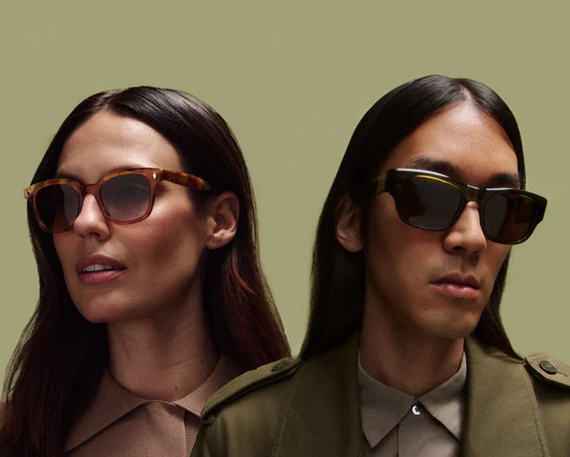 Two people with long dark hair wearing sunglasses from Vu pose against a light olive background. Showcasing Vu’s style, one wears brown tortoiseshell frames and the other black square frames from le plus grand inventaire de montures à Montréal.