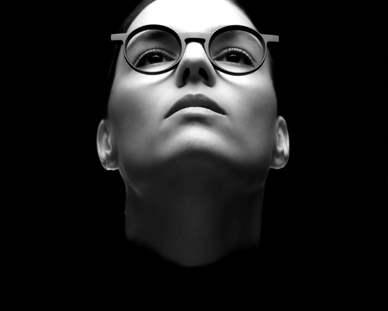 A black-and-white image of a person wearing glasses from Vu, looking upward with a serious expression, set against a dark background—showcasing the style found at la lunetterie à Montréal.