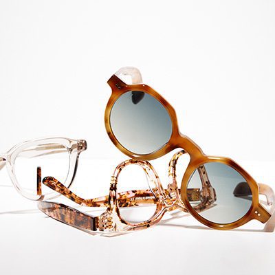 Trois paires de lunettes de Vu, une lunetterie à Montréal, sont disposées sur une surface blanche : monture transparente, motif écaille et solaires rondes aux verres teintés.