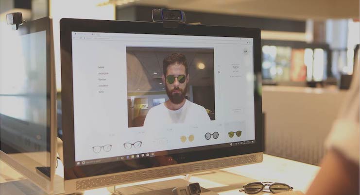 A computer screen displays Vu’s virtual try-on tool for eyeglasses, showing a man with a beard wearing virtual sunglasses. Several different options from le plus grand inventaire de montures à Montréal are visible on the website interface.